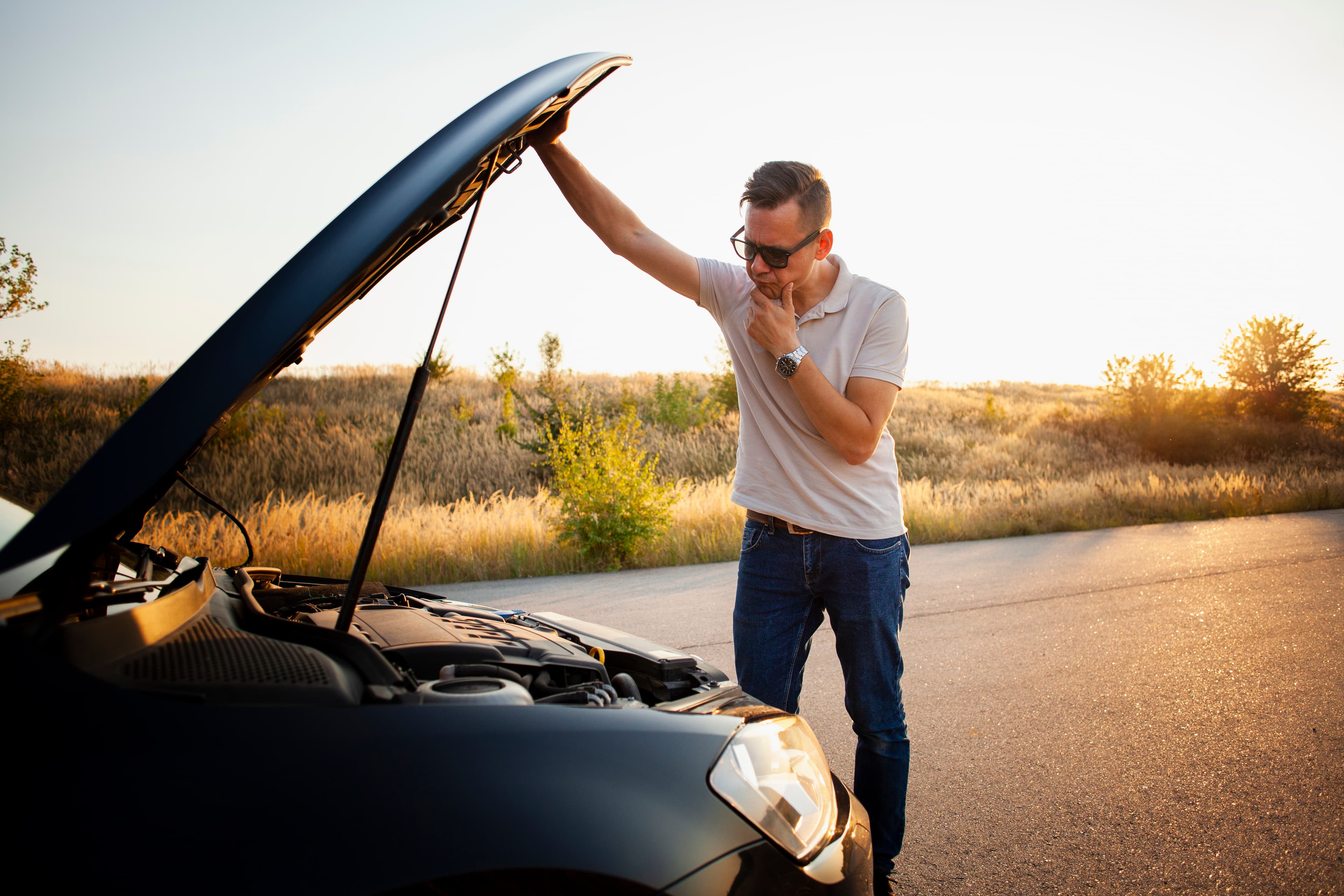 Homem esperando socorro em frente ao seu carro quebrado.